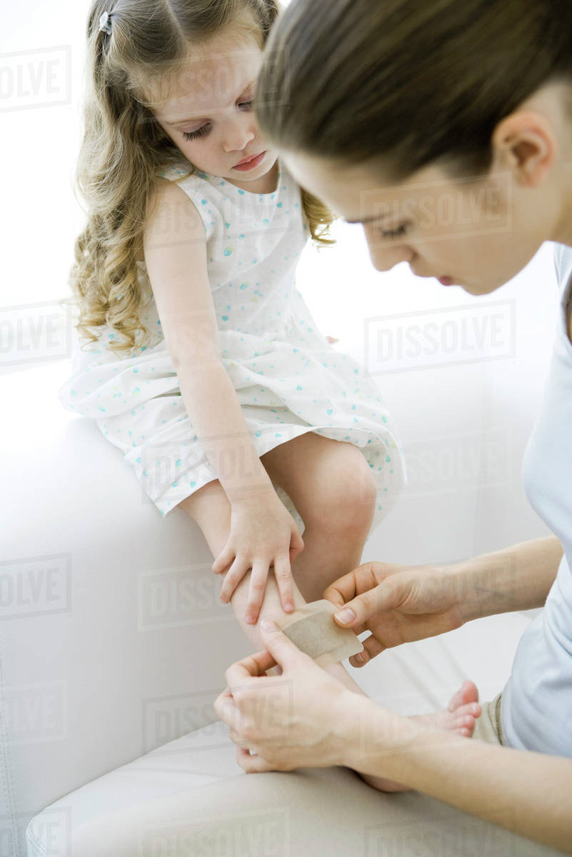 Mother putting adhesive bandage on young daughter's leg Stock Photo