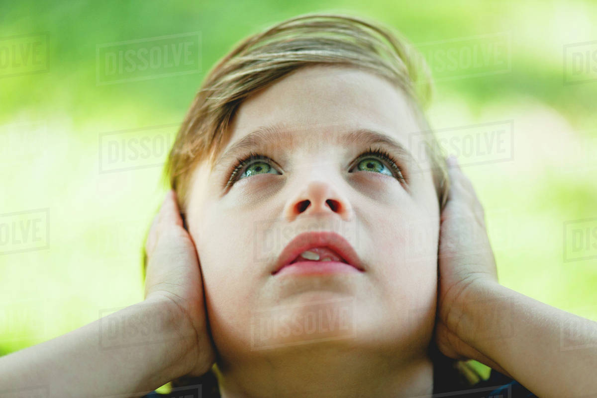 Boy covering ears with hands, looking up Stock Photo Dissolve