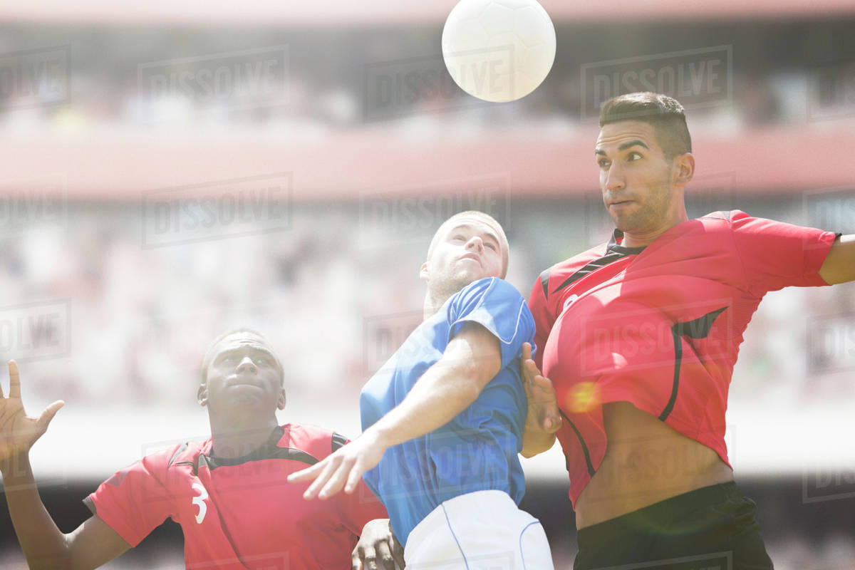 Soccer players jumping for ball on field Stock Photo Dissolve