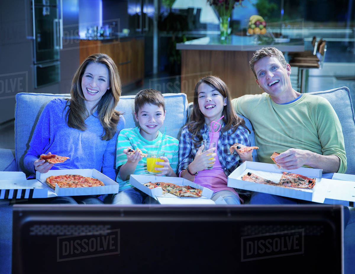 Family eating pizza in front of television in living room Stock Photo