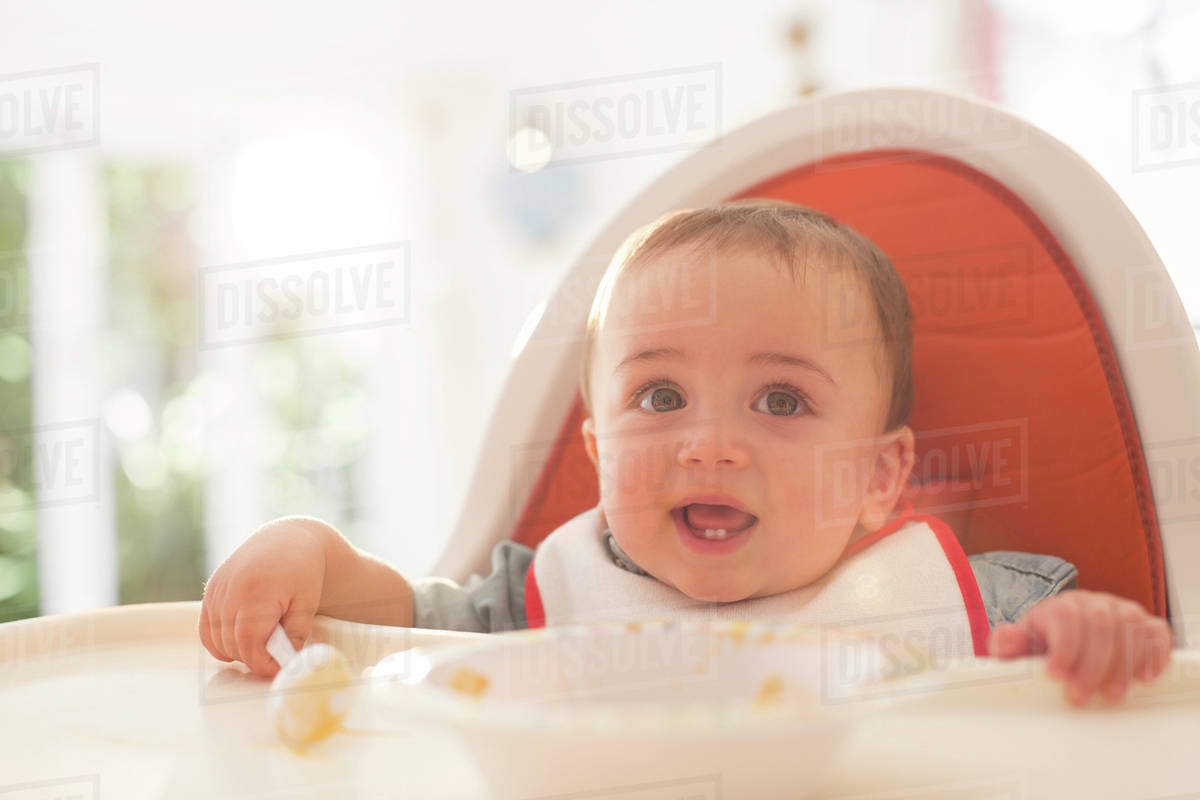 Baby boy eating in high chair Stock Photo Dissolve