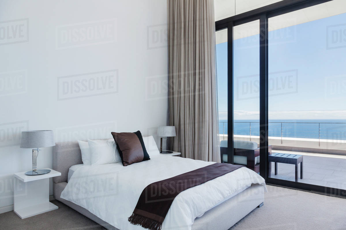 Bed and lamps in modern bedroom overlooking ocean Stock Photo Dissolve