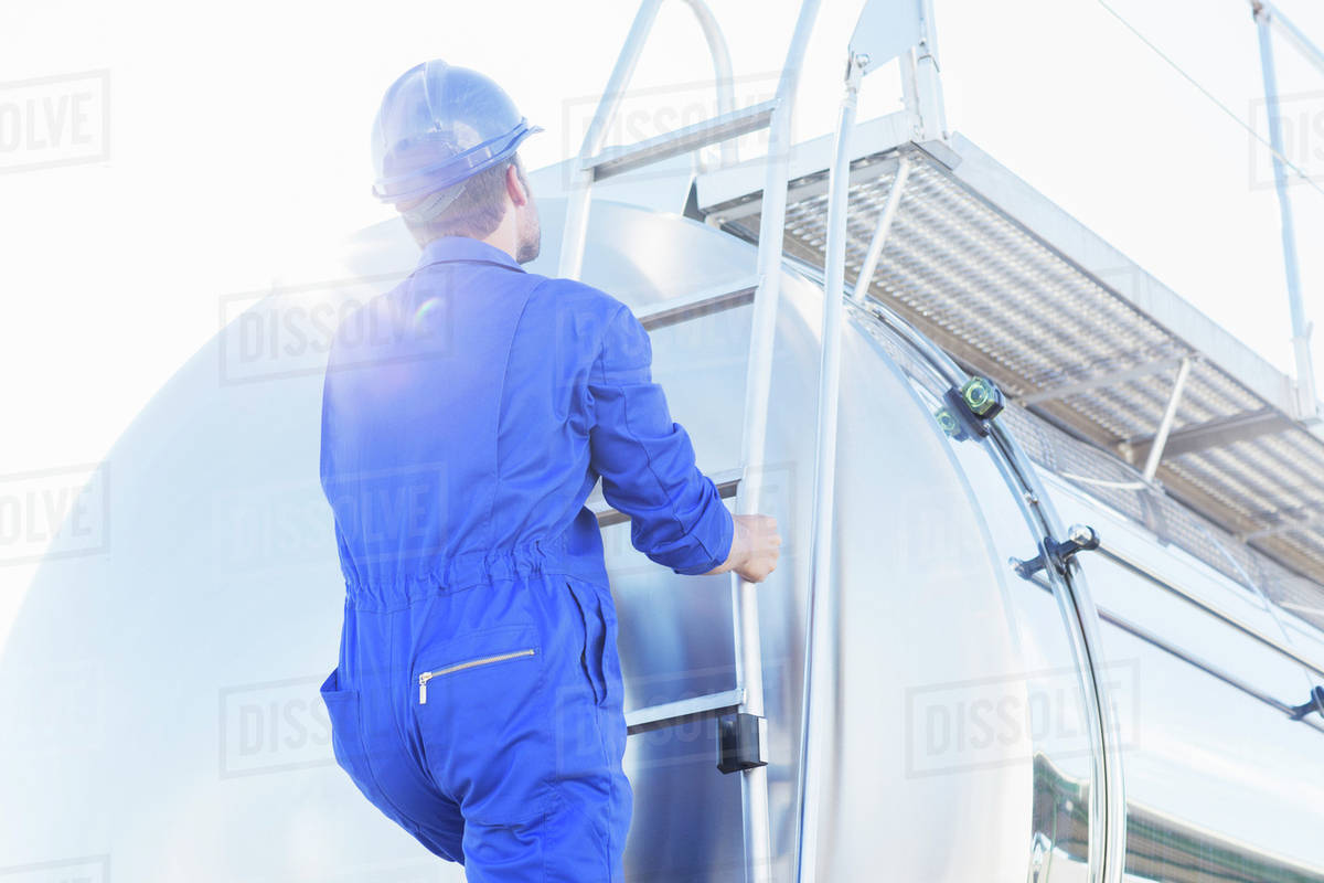 Worker climbing ladder at back of stainless steel milk tanker Stock