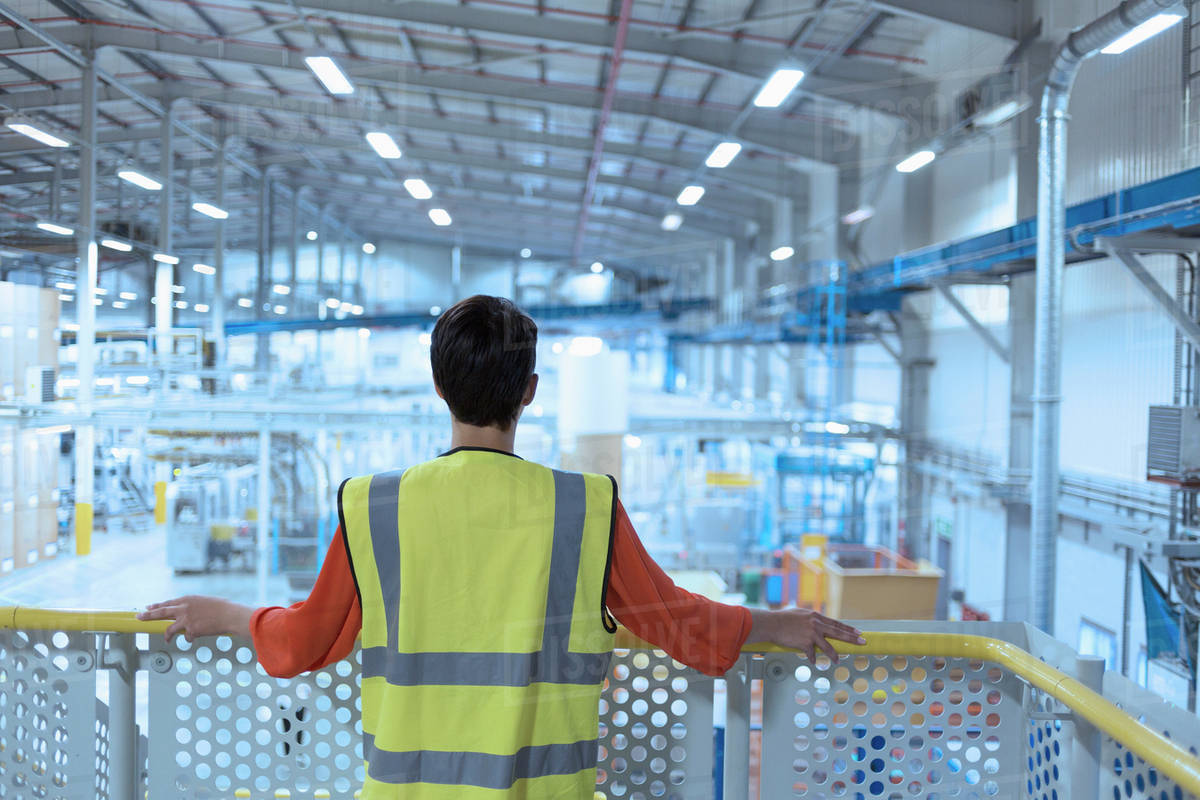 Worker in reflective clothing on platform looking out over factory