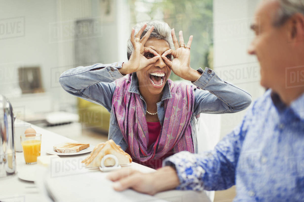 Playful mature woman gesturing finger glasses at breakfast table Royalty-free stock photo