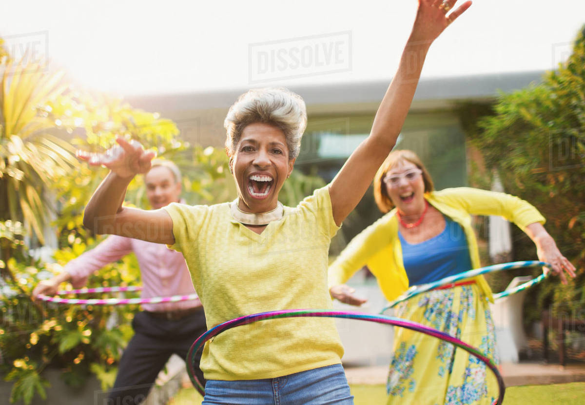 Portrait playful mature adults spinning with plastic hoops in garden Royalty-free stock photo