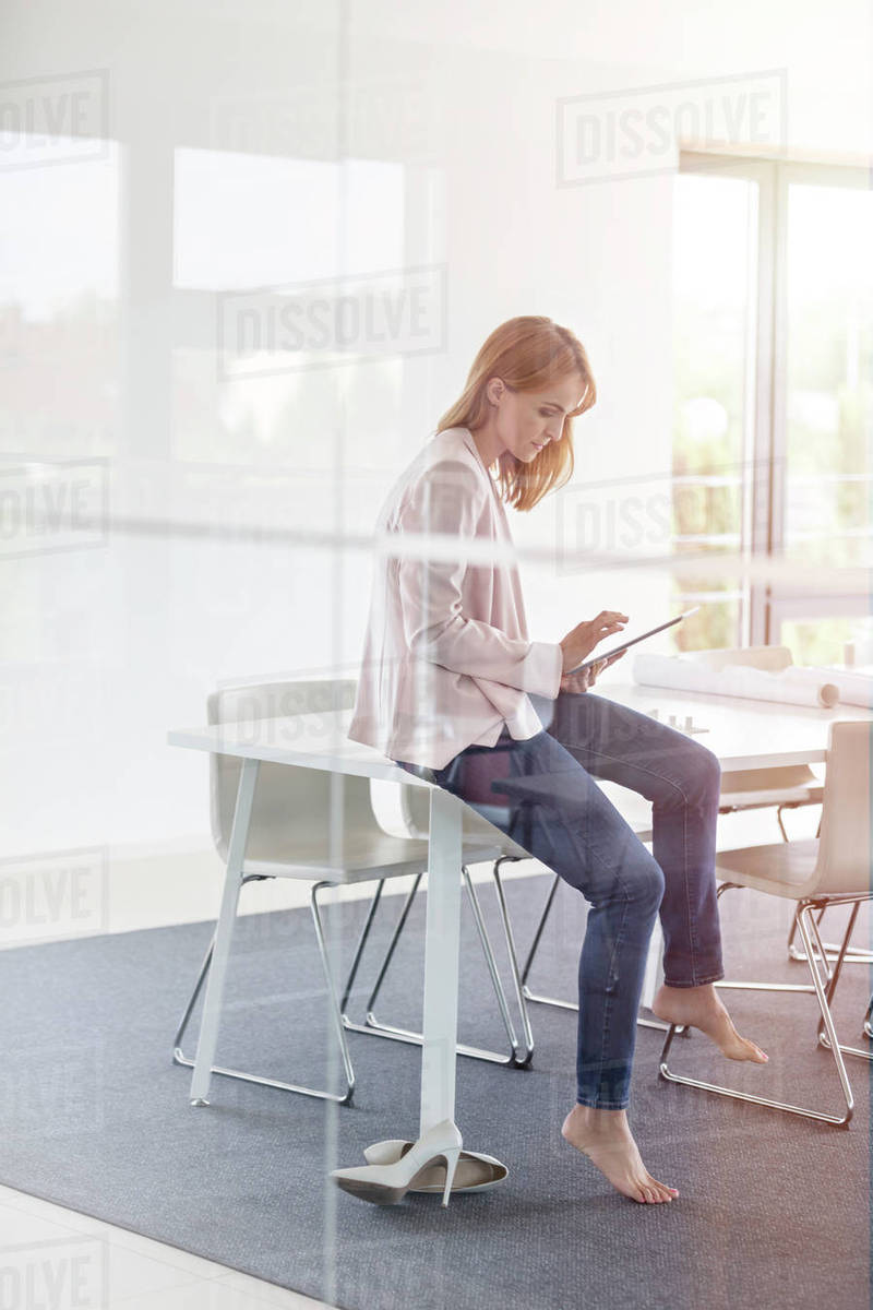 Barefoot businesswoman using digital tablet in conference room Stock