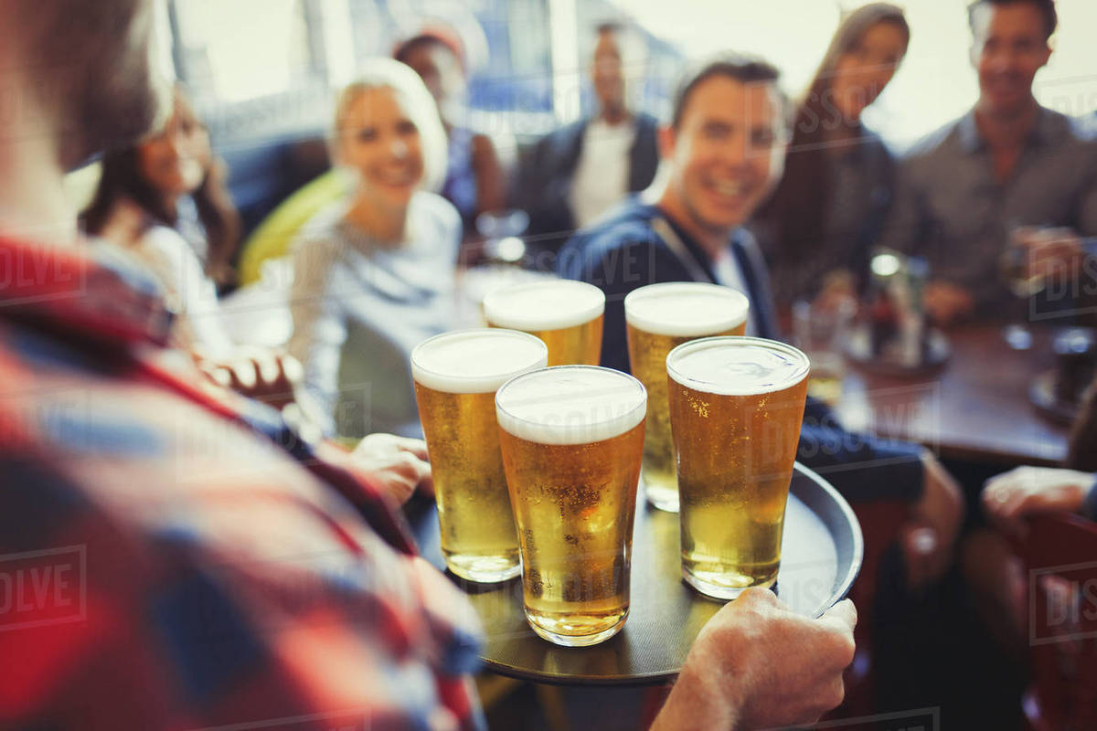 Bartender serving tray of beers to friends in bar Stock Photo Dissolve