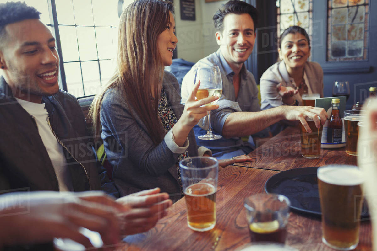 Friends drinking beer and wine and talking at table in bar Stock