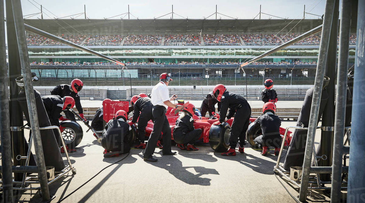 Manager and pit crew replacing tires on formula one race car in pit