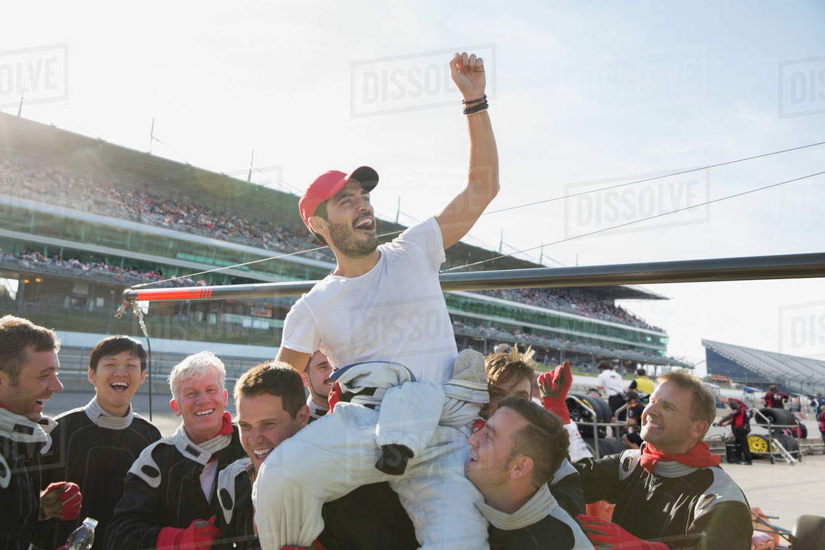 Formula one racing team carrying cheering driver on shoulders, celebrating victory on sports track Royalty-free stock photo
