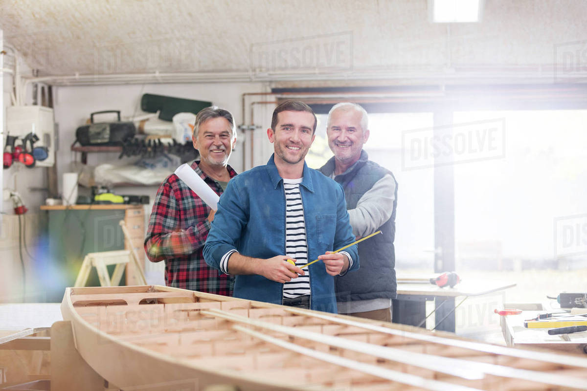 Portrait smiling male carpenters working at wood boat in