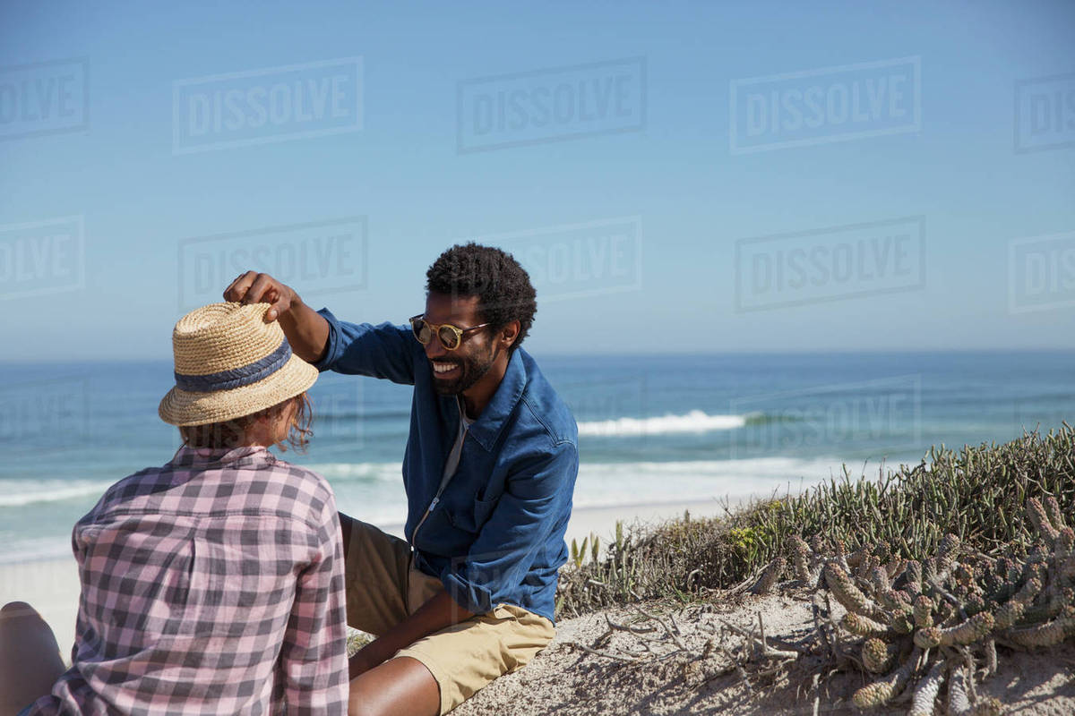 Smiling Man Placing Hat On Friend Sunny Summer Ocean Beach Smiling Man Placing Hat On Friend Sunny Summer Ocean Beach