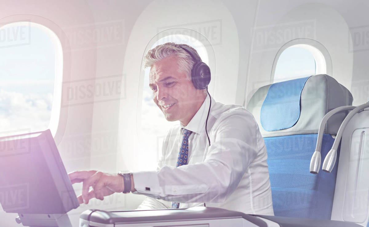 Businessman with headphones watching movie on airplane Stock Photo