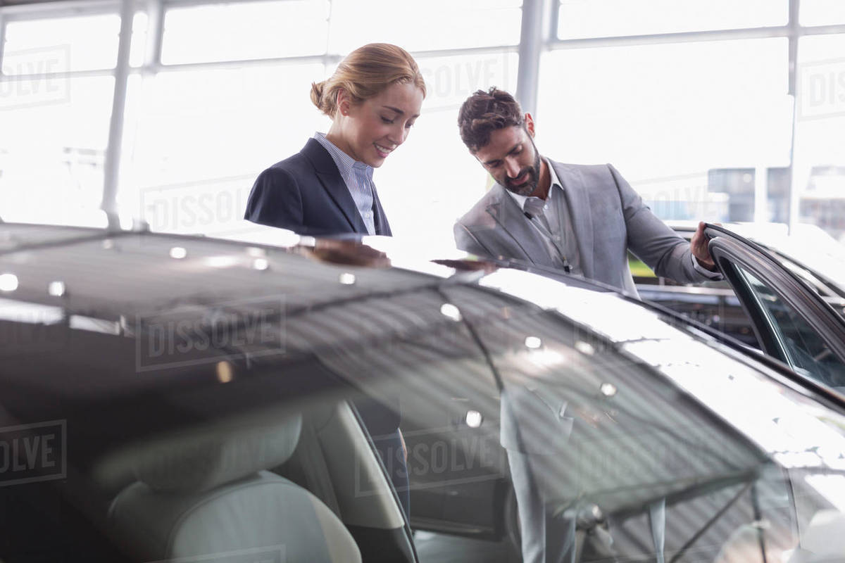 car salesman showing new car to female customer in car dealership car salesman