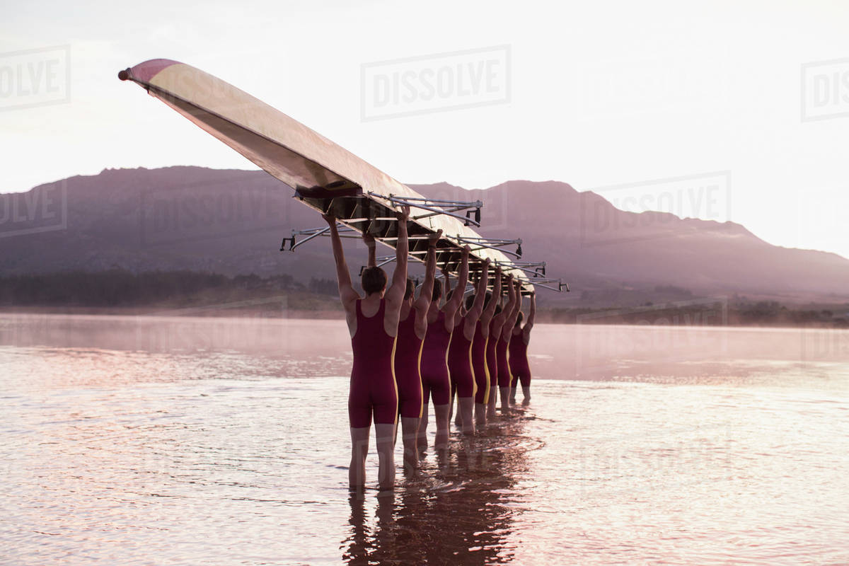 Rowing team carrying row boat overhead in still lake Stock Photo