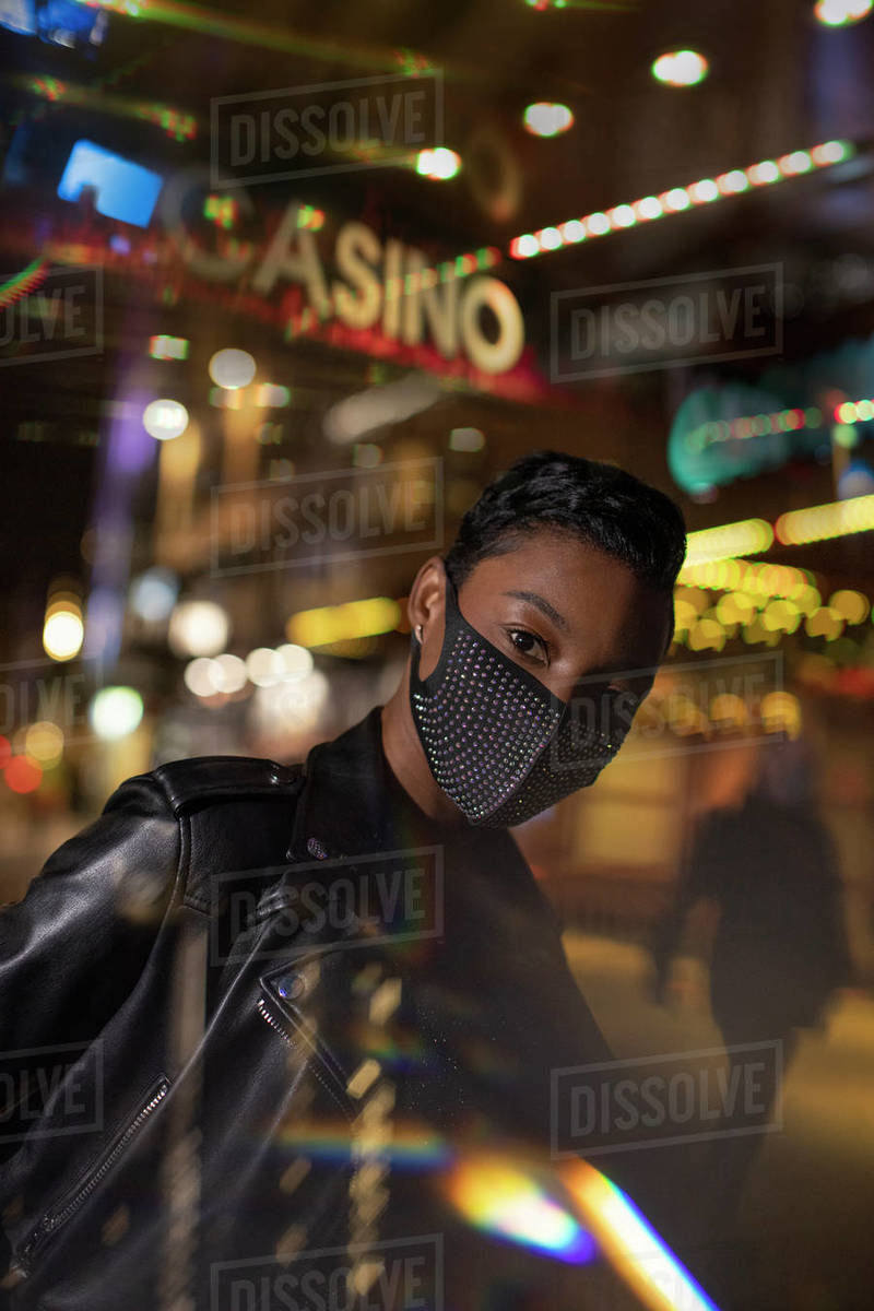 Portrait confident young woman in face mask on city street at night