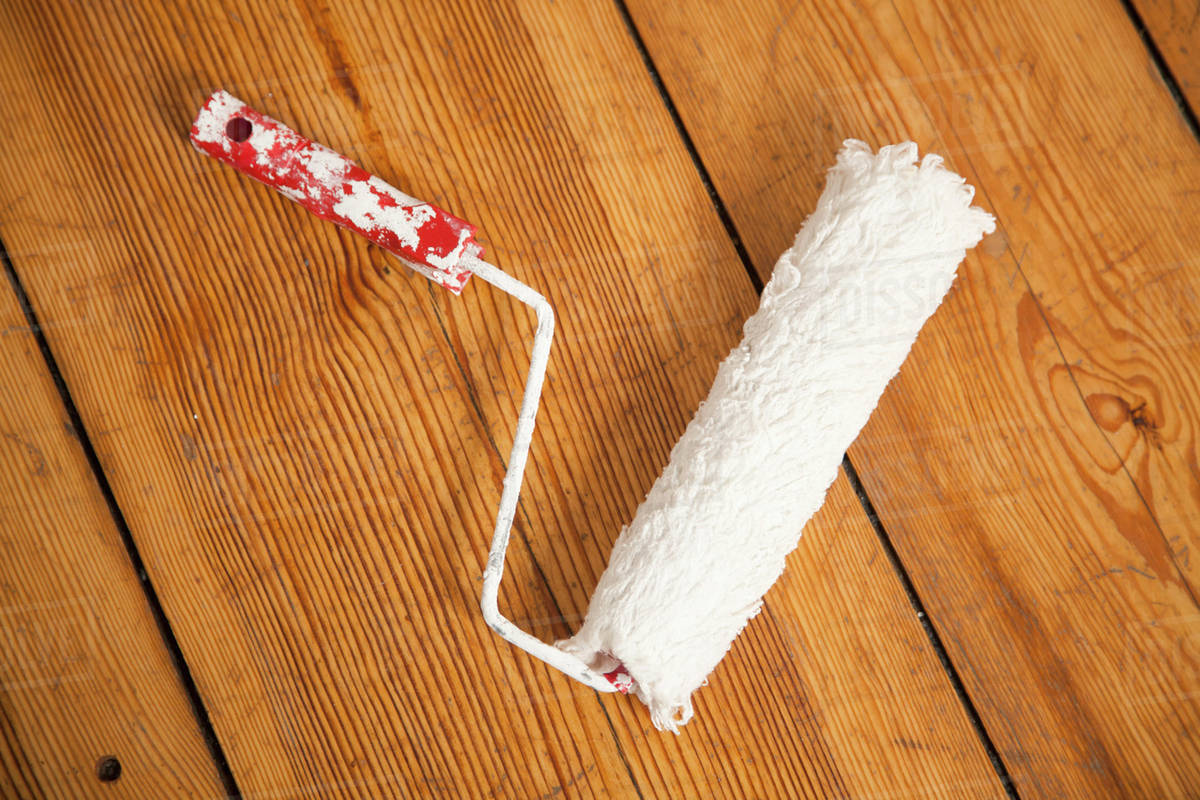 A paint roller on a hardwood floor, directly above Stock Photo Dissolve