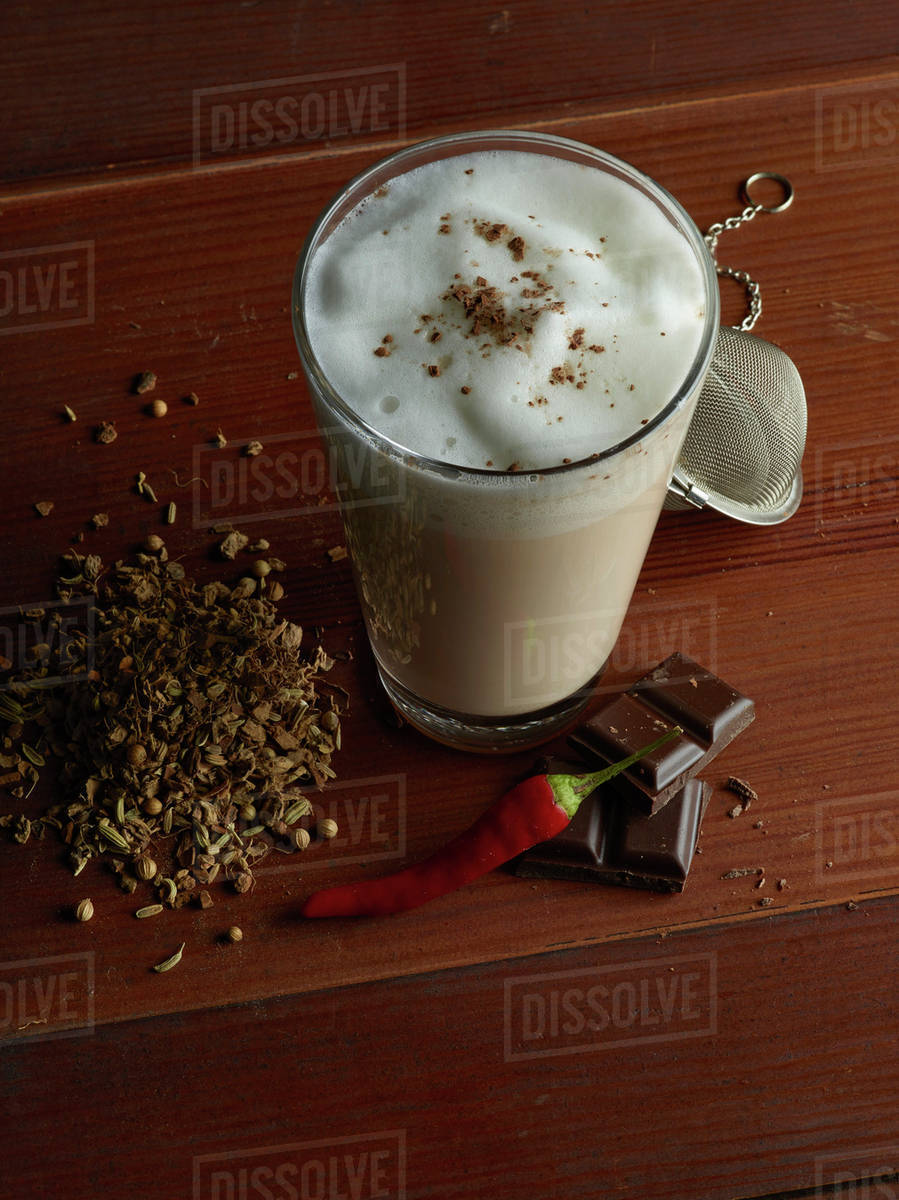 Chai latte surrounded by chocolate, chili, tea and spices Stock Photo