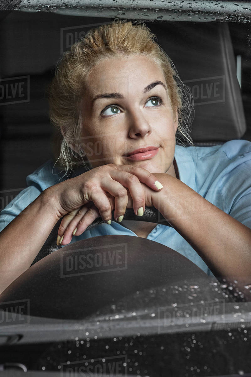 Thoughtful woman leaning on steering wheel in car Stock Photo Dissolve