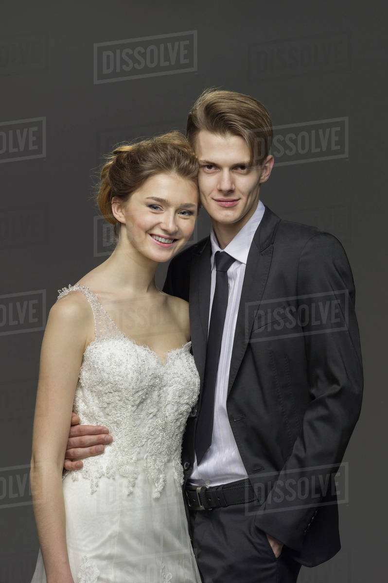 Portrait of happy newlywed couple standing against gray background