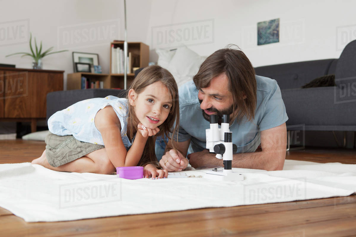 Father and daughter using microscope on carpet at home Stock Photo