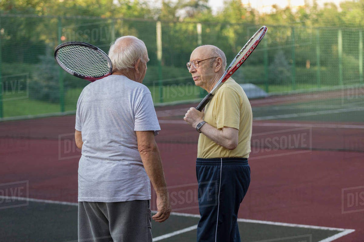 Senior friends carrying tennis rackets while talking at playing field