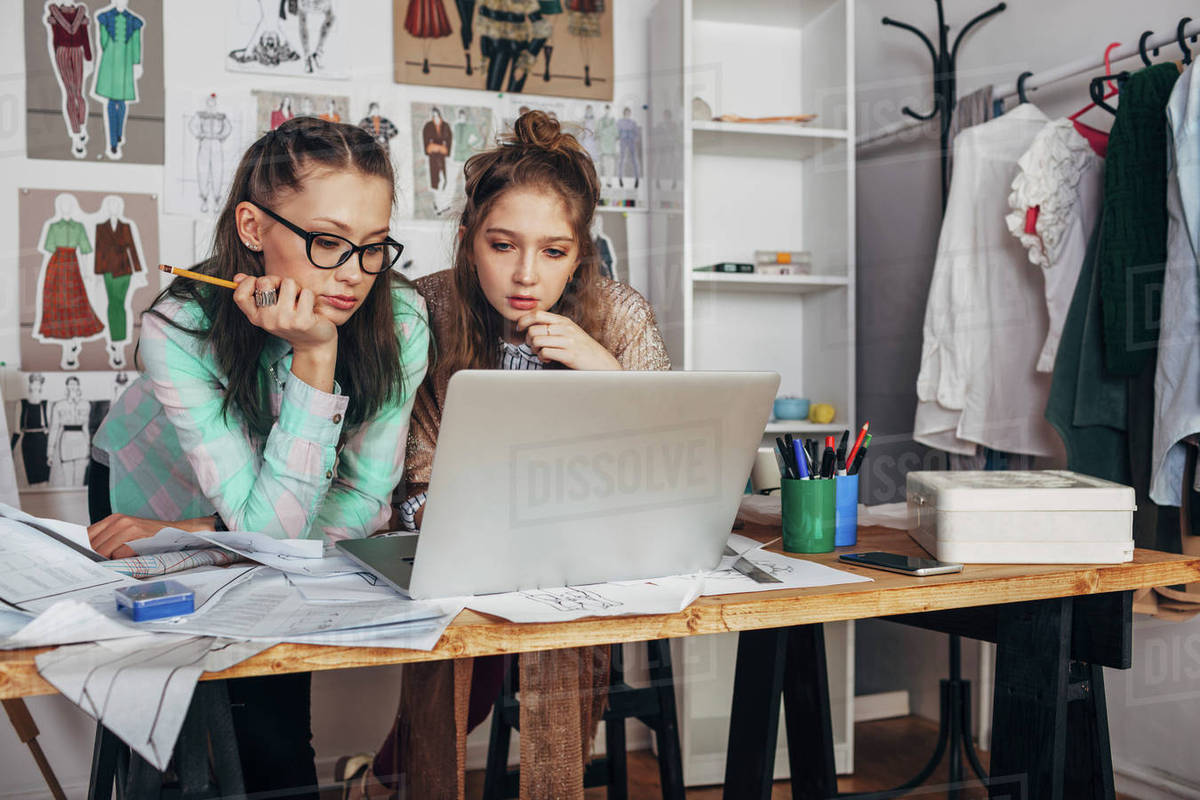 Female trainee and beautiful fashion designer using laptop on workbench
