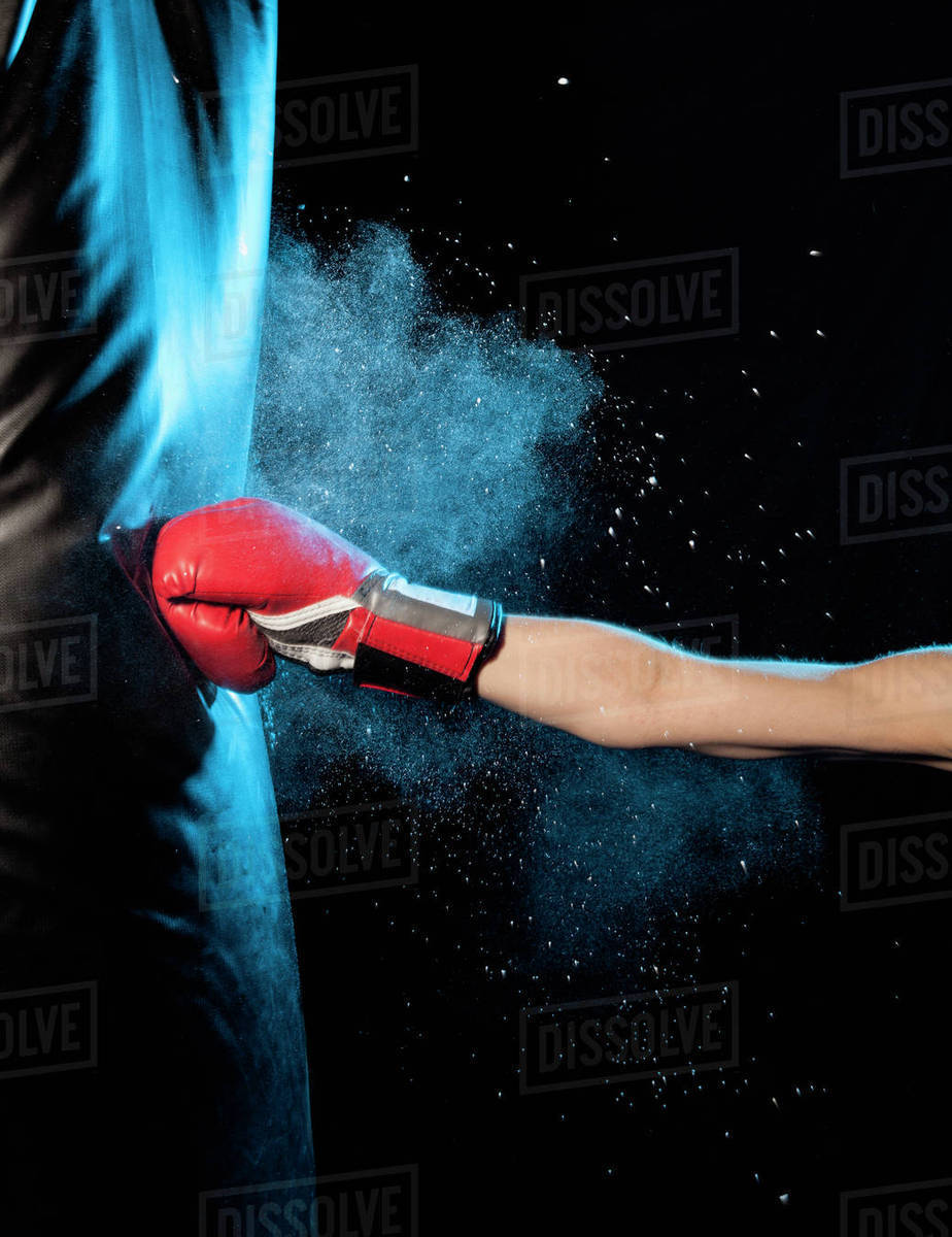 Cropped image of man hitting punching bag against black background Stock Photo Dissolve