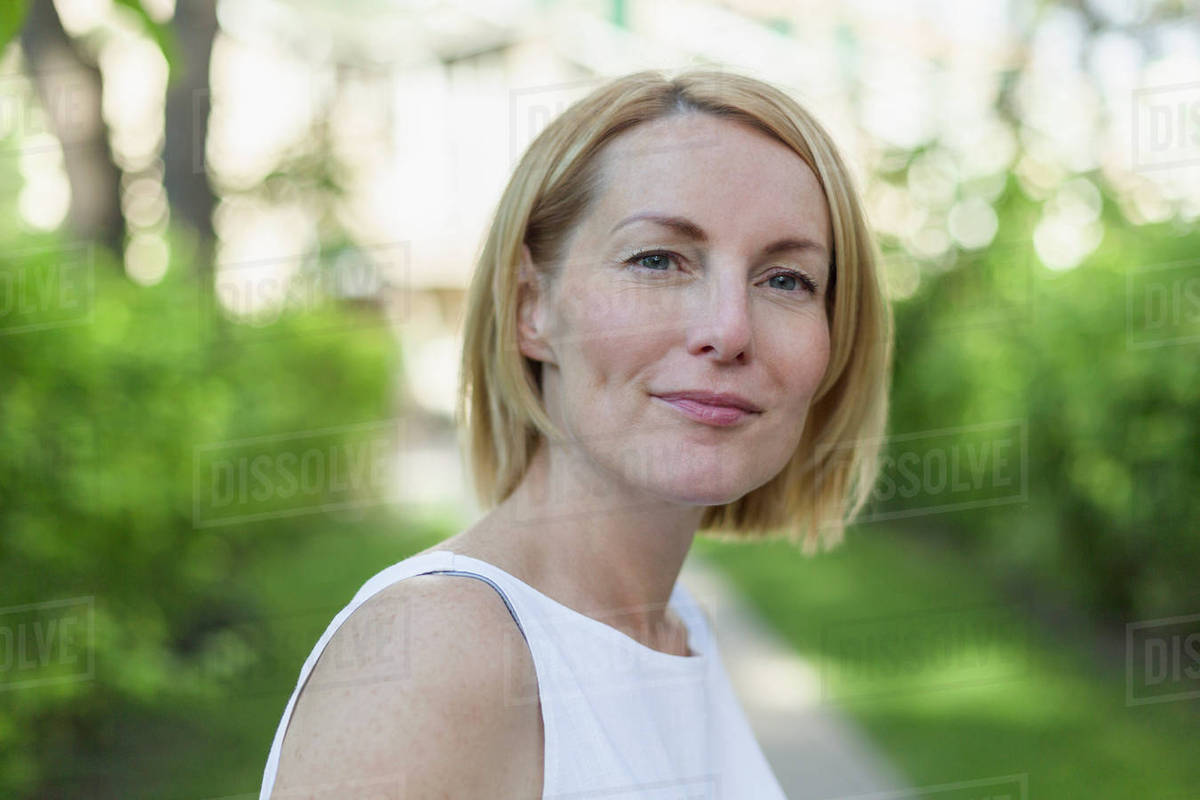 Close-up portrait of confident smiling mature woman with short blond hair at park Royalty-free stock photo