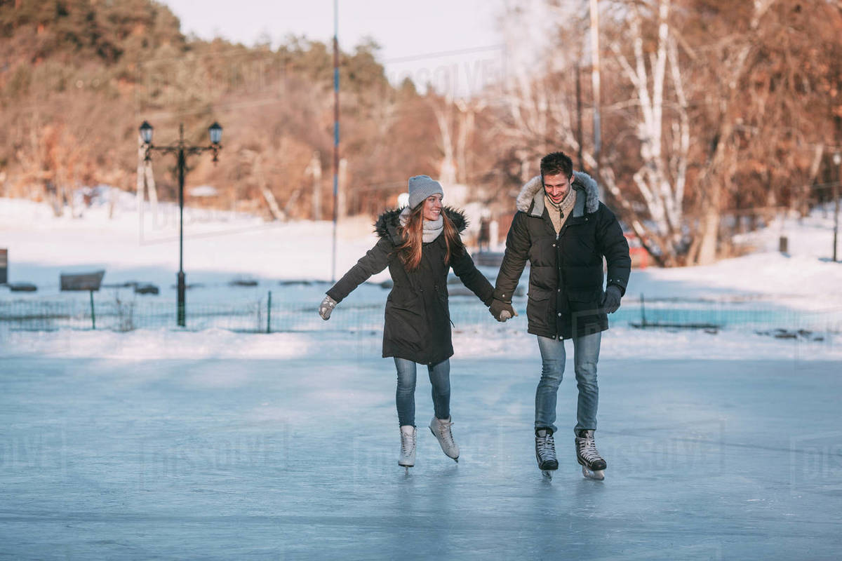 Full length of happy couple holding hands while enjoying iceskating on