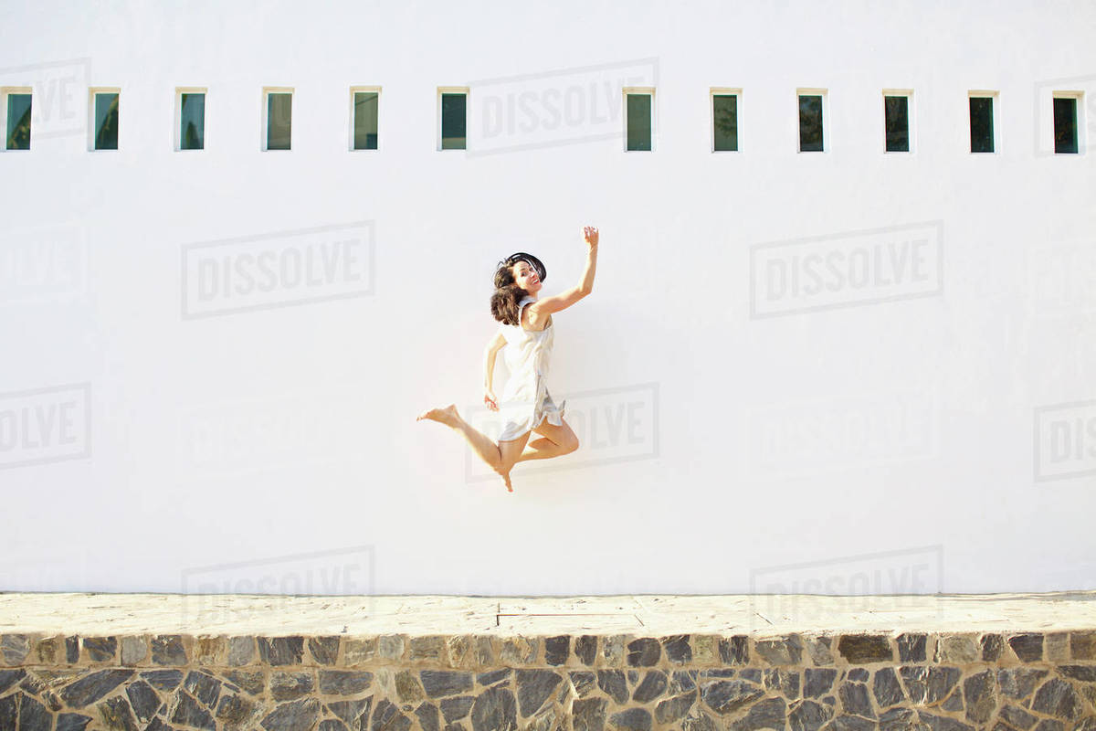 Portrait happy, carefree woman jumping for joy against sunny summer wall Royalty-free stock photo