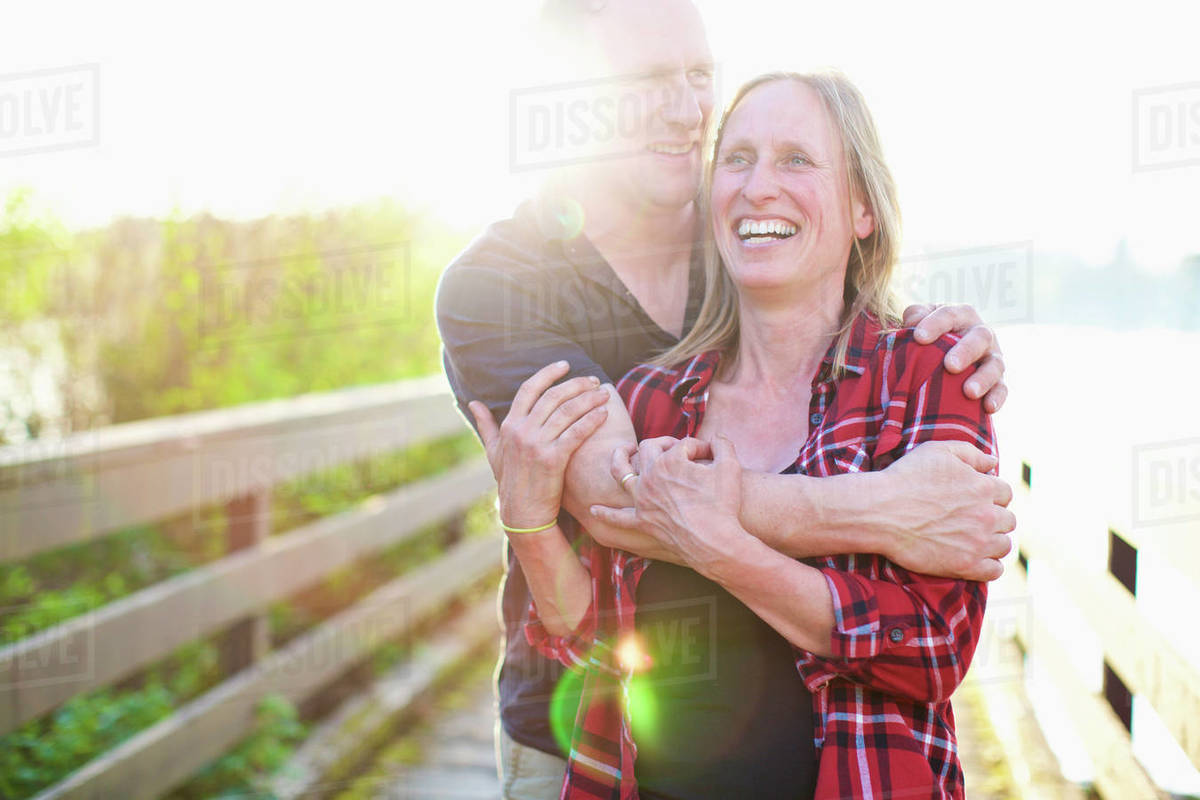 Portrait happy, affectionate couple hugging on sunny summer footbridge Royalty-free stock photo