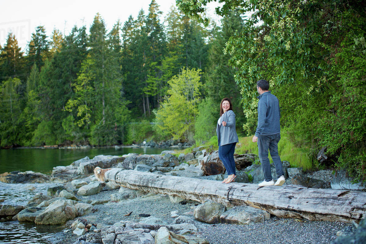 Happy couple walking on fallen log at lakeside in woods, Mill Bay, British Columbia, Canada Royalty-free stock photo