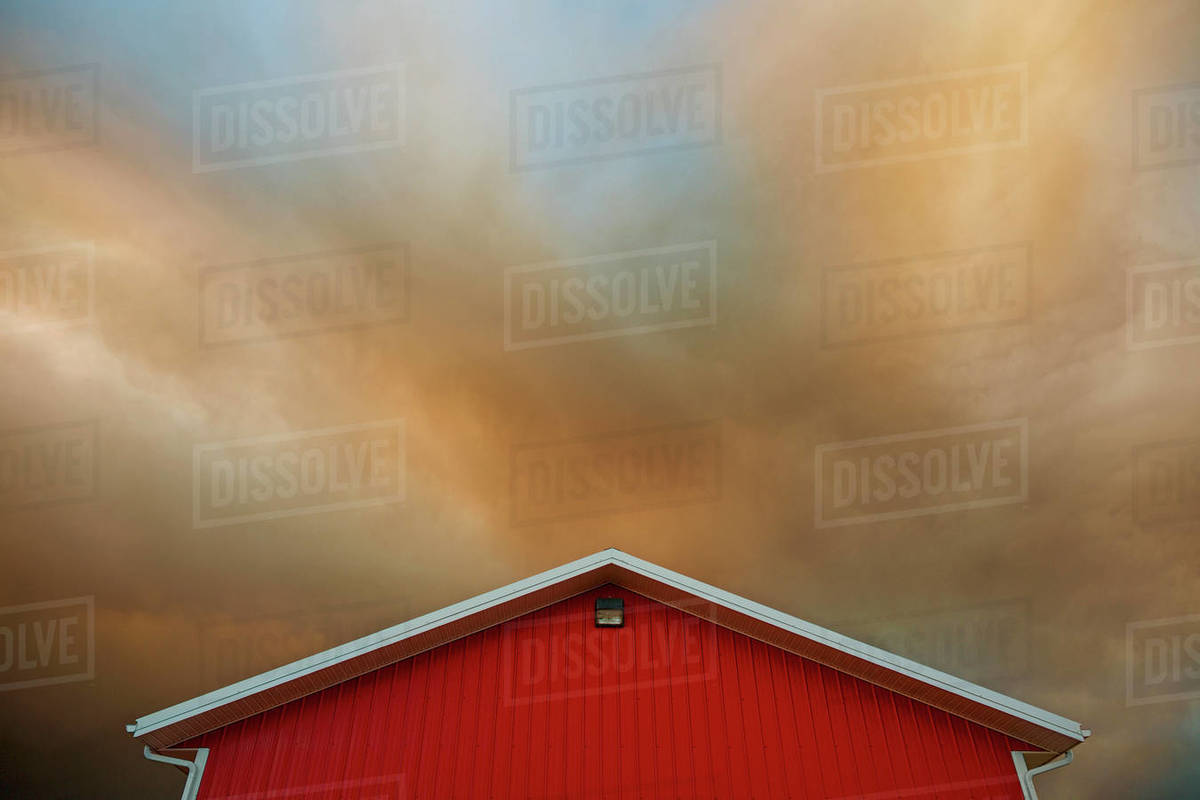 Orange clouds forming in dramatic sky over vibrant red barn Royalty-free stock photo