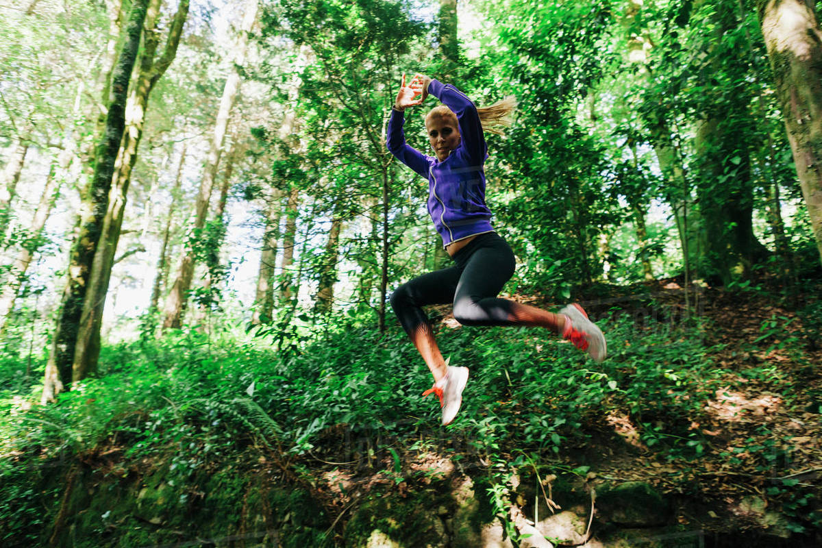 Portrait carefree female personal trainer hiking, jumping in forest Royalty-free stock photo