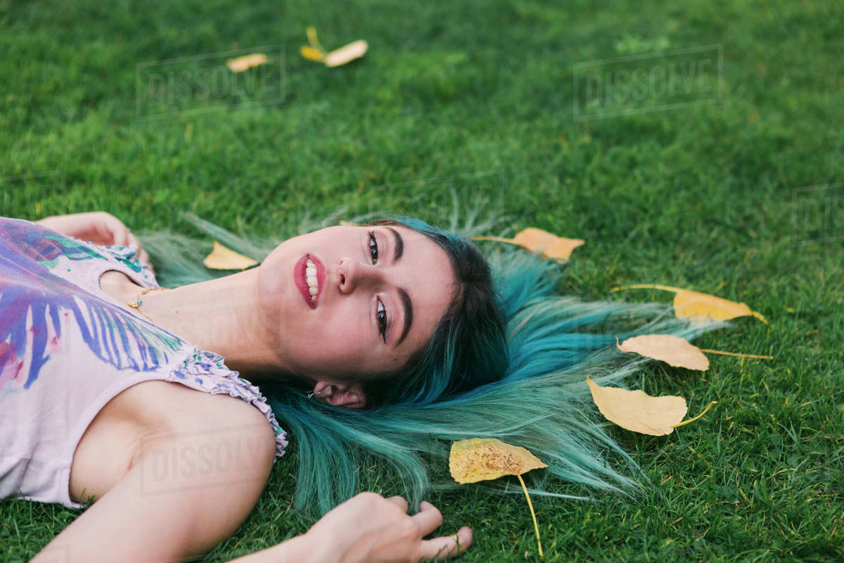Portrait serene young woman with blue hair laying in grass with autumn leaves Royalty-free stock photo