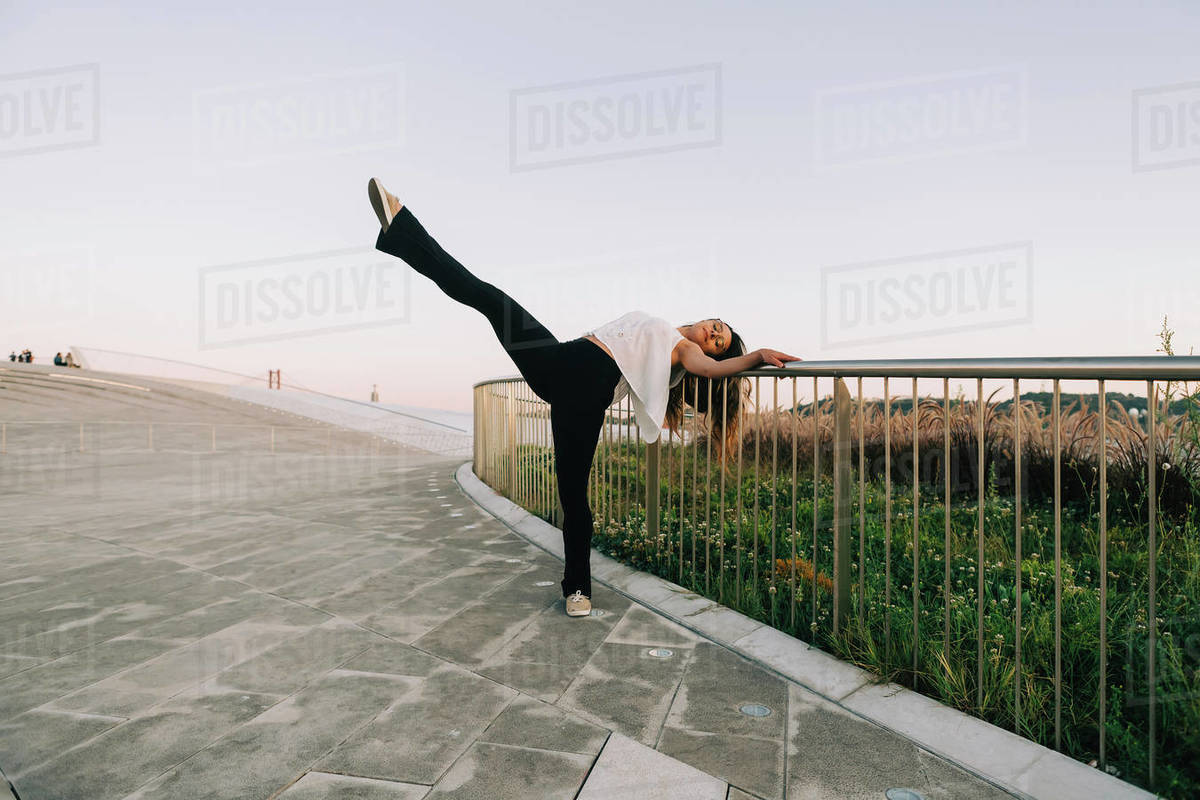 Portrait carefree young female dancer doing standing splits at park railing Royalty-free stock photo