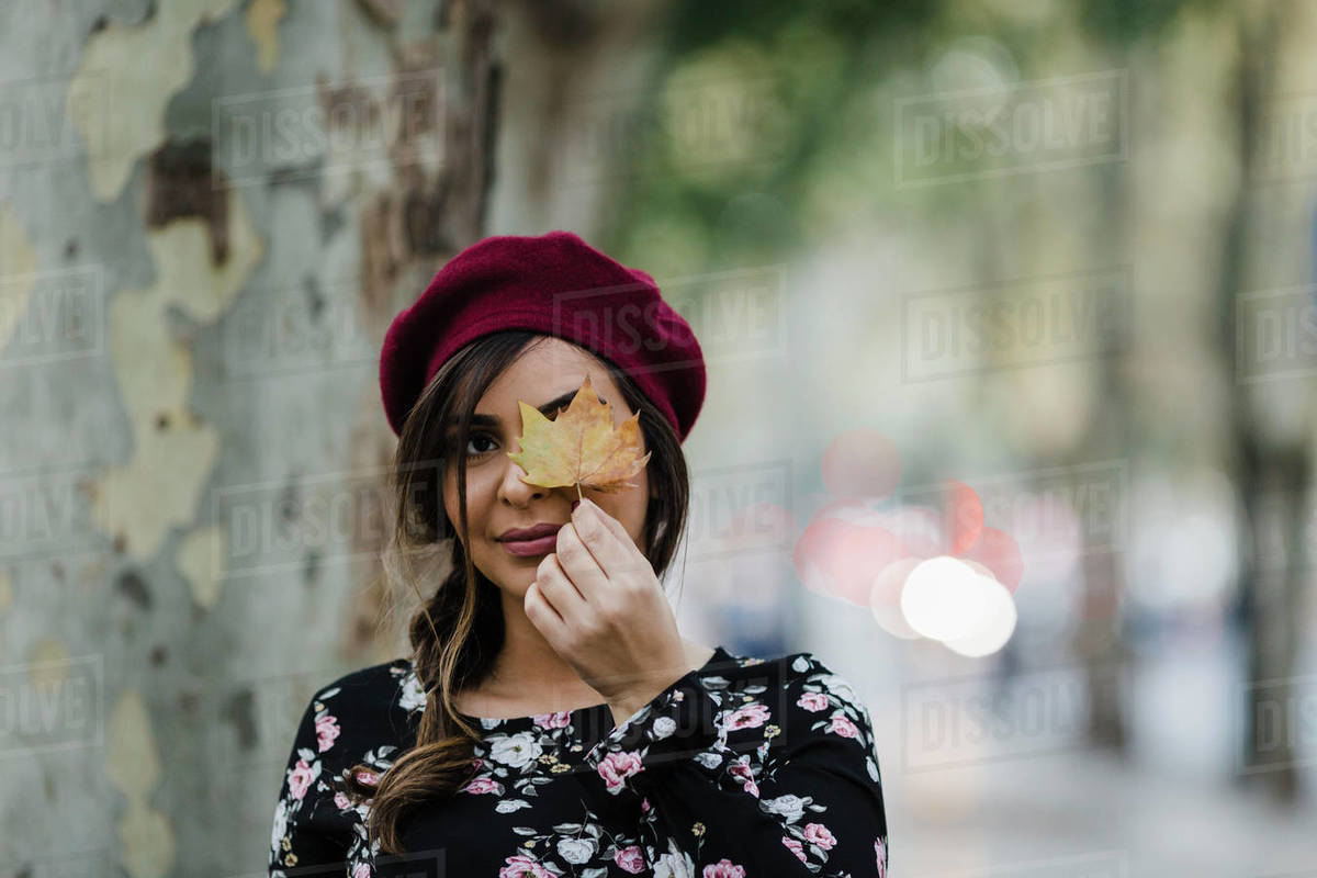 Portrait young woman in beret holding autumn leaf in park Royalty-free stock photo