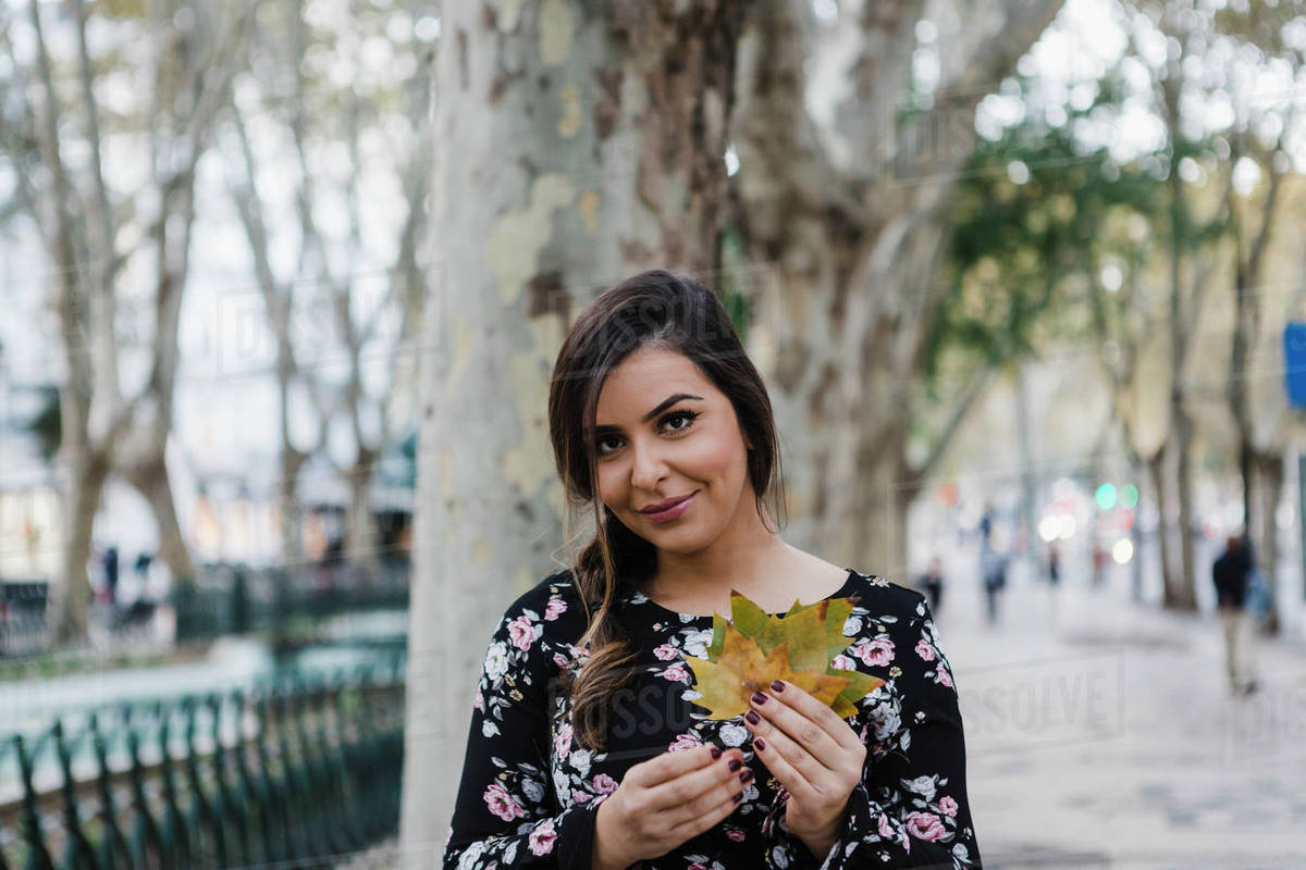 Portrait smiling young woman holding autumn leaves in urban park Royalty-free stock photo