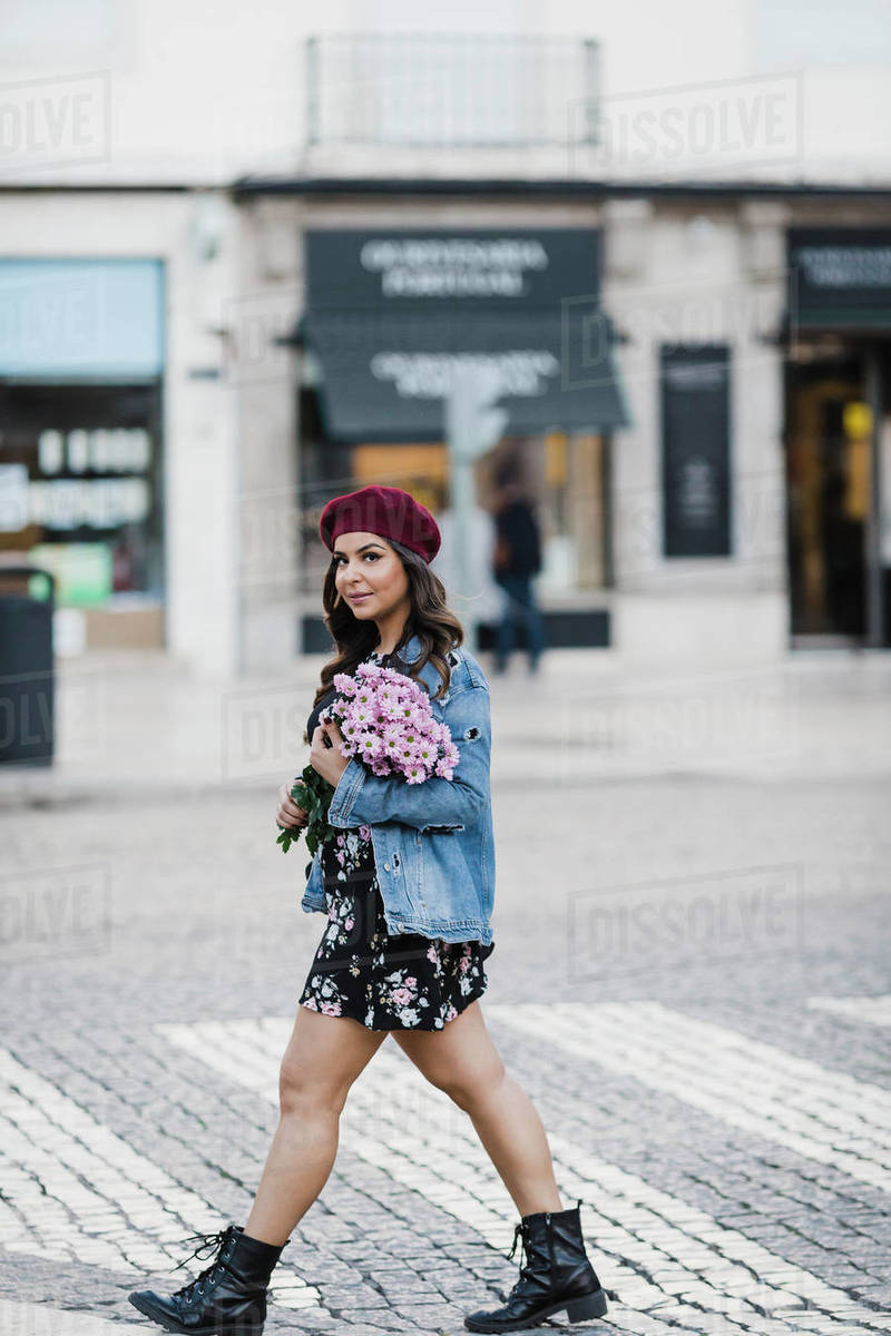 Portrait confident young woman crossing city street with bouquet of flowers Royalty-free stock photo