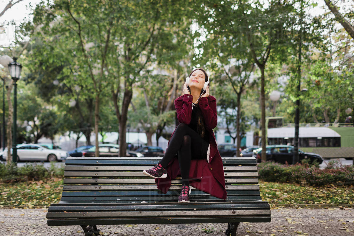 Carefree woman listening to music with headphones on urban park bench Royalty-free stock photo