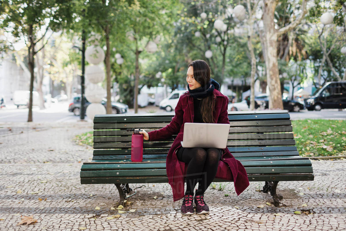 Woman with water bottle working at laptop in autumn city park Royalty-free stock photo